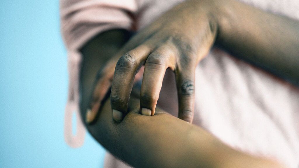 Close up of an African American woman scratching their arm.