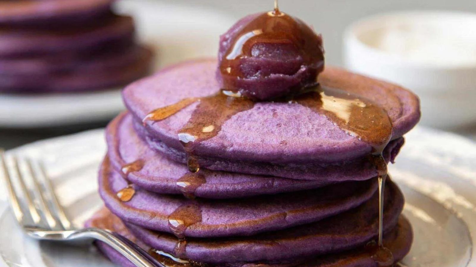 Ube Pancakes on a plate with syrup being drizzled on top.