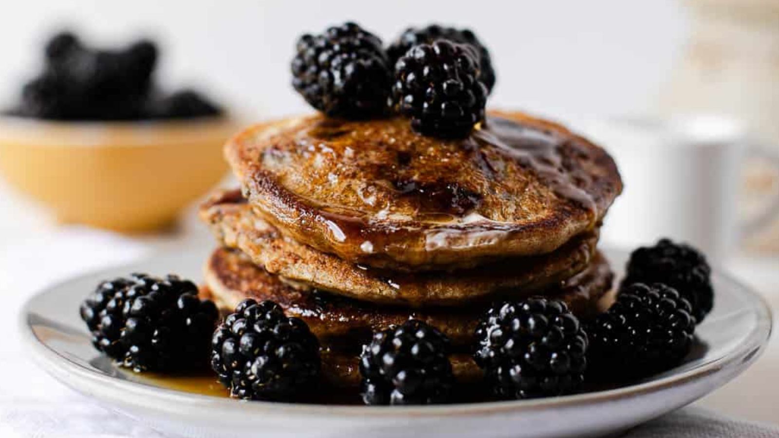 Whole Wheat Blackberry Pancakes stacked on a plate with blackberries.