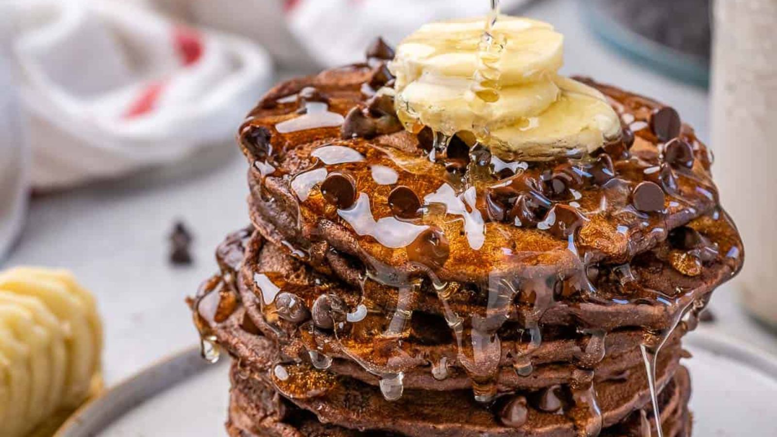 Chocolate Oatmeal Pancakes stacked on a plate with syrup being drizzled.
